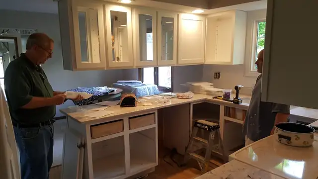 Nu-Look Kitchens installers fitting white cabinets with glass-front uppers above new light stone countertops